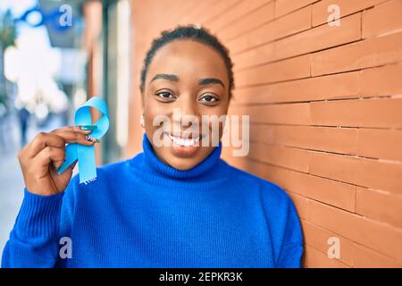 Junge afroamerikanische Frau lächelnd glücklich hält blauen Bekanntheitsband an der Stadt. Stockfoto