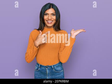 Junge lateinische transsexuelle Transgender Frau in lässiger Kleidung erstaunt und lächelnd auf die Kamera, während mit der Hand und zeigen mit dem Finger präsentieren. Stockfoto