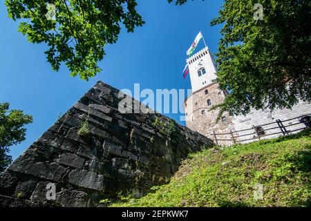 Uhrturm der Burg von Ljubljana mit Stadtflagge und einem Teil der Mauern sichtbar, Slowenien Stockfoto