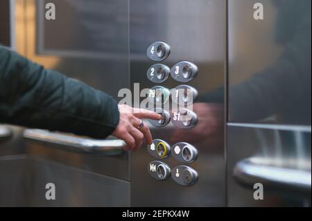 Detail einer Frau, die einen Knopf auf einem Aufzug drückt Auf den Boden gehen Stockfoto