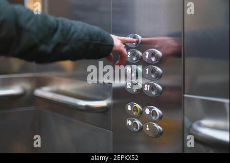 Detail einer Frau, die einen Knopf auf einem Aufzug drückt Auf den Boden gehen Stockfoto