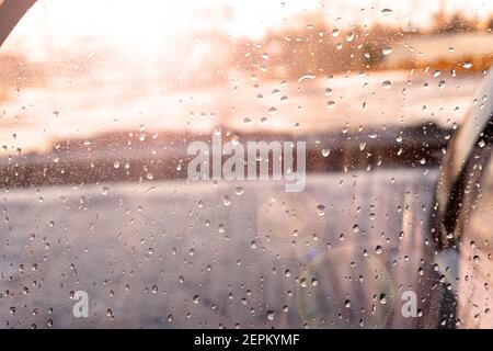 Wassertropfen, Regen klebt an der Fensterscheibe des Autos mit Aufflackern Stockfoto