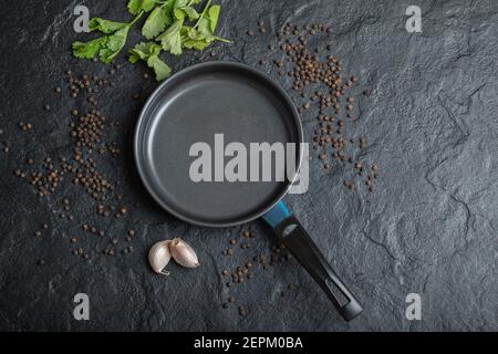 Draufsicht auf leere Bratpfanne über schwarzem Hintergrund mit Knoblauch und Paprika Stockfoto