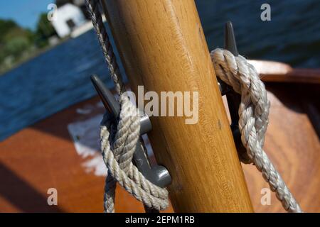 Nahaufnahme der Stollen auf dem Holzmast eines kleinen Segelbootes (Dinghy): Seile (Halyards) in lockeren Knoten gebunden, ein See oder Fluss im Hintergrund Stockfoto