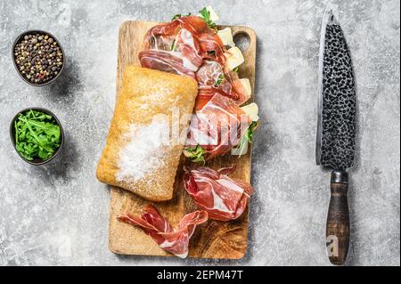 Ciabatta-Sandwich mit Schinken-Crudo-Schinken, Rucola und Camembert-Brie-Käse. Grauer Hintergrund. Draufsicht Stockfoto