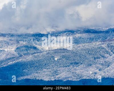 Die schneebedeckten Wälder an der Seite des Mt. Kosha mit Wolken um den Gipfel von Yamanouchi aus gesehen, Präfektur Nagano, Japan. Stockfoto