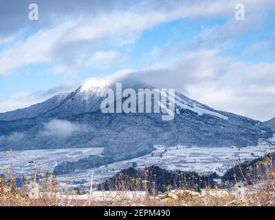 Die schneebedeckten Wälder an der Seite des Mt. Kosha mit Wolken um den Gipfel von Yamanouchi aus gesehen, Präfektur Nagano, Japan. Stockfoto