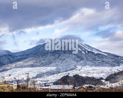 Die schneebedeckten Wälder an der Seite des Mt. Kosha mit Wolken um den Gipfel von Yamanouchi aus gesehen, Präfektur Nagano, Japan. Stockfoto