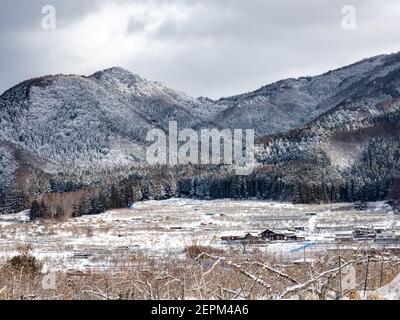 Die schneebedeckten Wälder an der Seite des Mt. Kosha mit Wolken um den Gipfel von Yamanouchi aus gesehen, Präfektur Nagano, Japan. Stockfoto