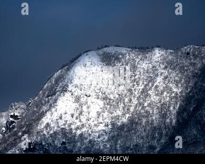 Die schneebedeckten Wälder auf dem Gipfel des Mt. Kosha mit Wolken um den Gipfel von Yamanouchi aus gesehen, Präfektur Nagano, Japan. Stockfoto