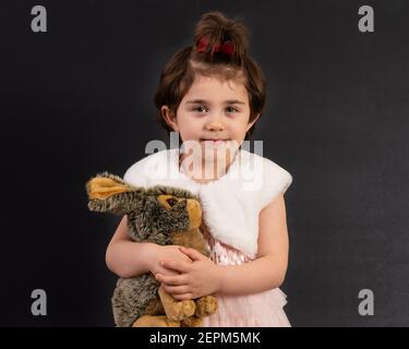 Lächelndes junges Mädchen hält Plüsch Häschen isoliert auf schwarz. Stockfoto