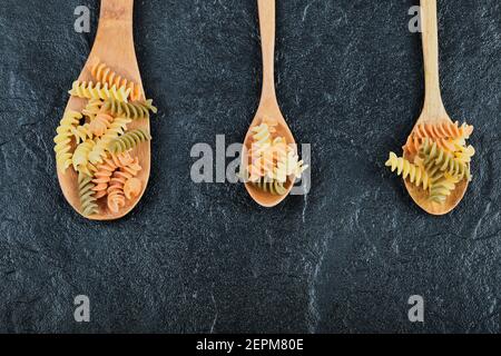 Verschiedene ungekochte Pasta auf Holzlöffeln auf dunklem Hintergrund Stockfoto