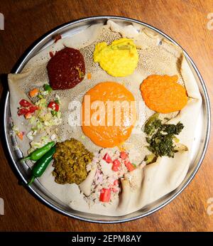 Äthiopier genießen ein traditionelles Injera-Gericht mit verschiedenen Gemüsesorten und Saucen. Stockfoto