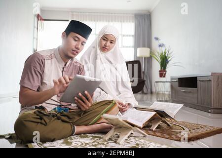 Asiatische muslimische Mann Lehre Frau Lesen Koran oder Koran im Wohnzimmer. muslim Paar zu Hause beten Stockfoto