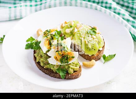 Vegetarisches Frühstück. Sandwich mit Avocado-Püree, gekochten Eiern und Sandwich-Frischkäse, Kiwi, Nüssen. Gesundes Frühstück oder Mittagessen. Stockfoto