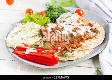 Gegrillter Hähnchenkebab mit Pita, frisches Gemüse auf einem weißen Tisch. Gegrillte Fleischspieße, Shish Kebab auf weißem Hintergrund. Stockfoto