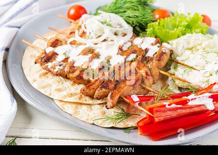 Gegrillter Hähnchenkebab mit Pita, frisches Gemüse auf einem weißen Tisch. Gegrillte Fleischspieße, Shish Kebab auf weißem Hintergrund. Stockfoto