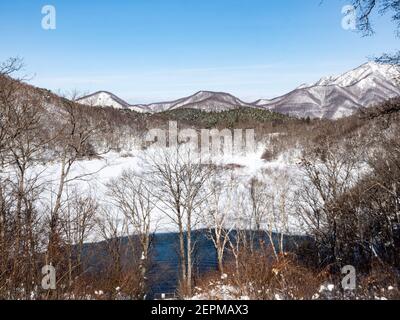 Die schneebedeckten Wälder der Japanischen alpen im Blick Ein meist gefrorener biwa-ike See im Winter in der Nähe der Shiga Skigebiet Kogen in Nagano Präfekt Stockfoto