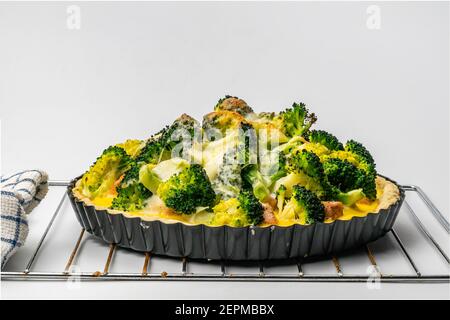 Blick auf frisch gebackenen hausgemachten Brokkoli Lachs Quiche in Metall Ofen Kuchen Backplatte auf weißem Hintergrund. Stockfoto