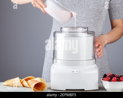 Eine kaukasische Frau gießt hausgemachte, natürliche Eiscreme-Mischung in eine Eismaschine. Beeren und Erdbeeren wurden hinzugefügt, um Geschmack hinzuzufügen. Stockfoto