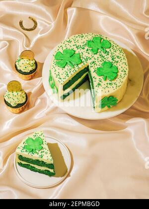 St. Patricks Day Süßes Essen Konzept. Süße Desserts für die St. Patrick's Day Party - kuchenverzierte Kleeblätter, grüne Samt-Cupckakes, Schokoladen-Goldmünzen und Hufeisen auf Satin. Speicherplatz kopieren. Vertikal Stockfoto