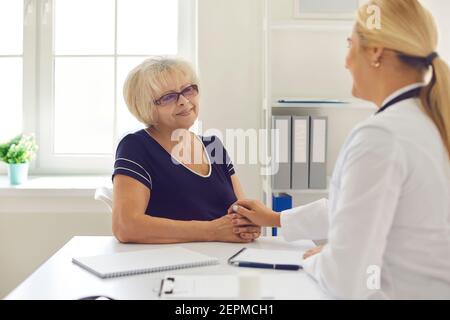 Junge Frau Arzt berühren Senior positive Frau Patienten Hände während Besuch in der Klinik Stockfoto