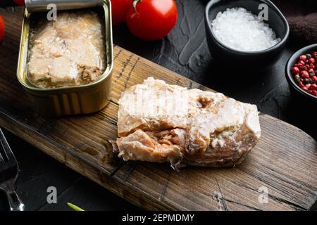 Set aus Wildrosa Lachs aus der Dose, auf Holzschneidebrett, auf schwarzem Hintergrund mit Kräutern und Zutaten Stockfoto