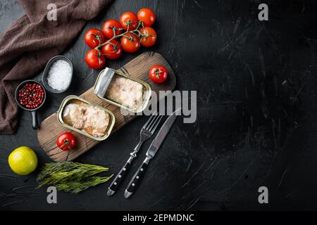 Dosen Wild Pink Lachs Set, auf Holzschneidebrett, auf schwarzem Hintergrund mit Kräutern und Zutaten, Draufsicht flach legen, mit Copyspace und Platz für Stockfoto
