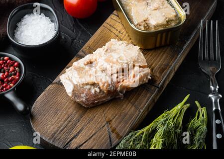 Dosen Wild Alaska Lachs Set, auf Holzschneidebrett, auf schwarzem Hintergrund mit Kräutern und Zutaten Stockfoto