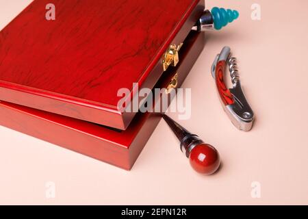 Geschenkset mit Korkenzieher und abnehmbaren Deckeln. Weinkorken und Flaschenöffner in einer Holzkiste auf rosa Hintergrund. Stockfoto