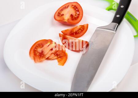 Auf einem Schneidebrett befindet sich eine frische, rot geschnittene Tomate und ein großes Kochmesser. Auf einem isolierten weißen Hintergrund. Stockfoto