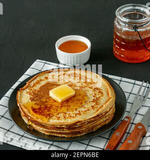 Pfannkuchen mit Honigsirup und Butter auf einem dunklen Teller serviert. Traditionelle Crepes für Pancake Week oder Shrovetide Stockfoto