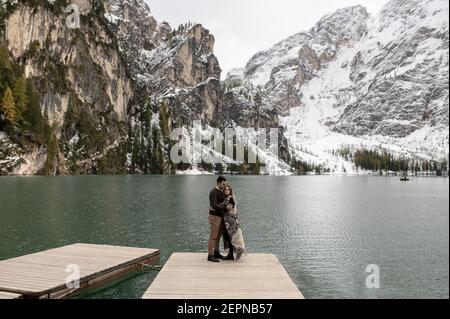 Voller Körper von liebevollen sanften Paar umarmt sich gegenseitig auf Hölzerne Pier gegen Lago di Prags See von verschneiten umgeben Berge Stockfoto