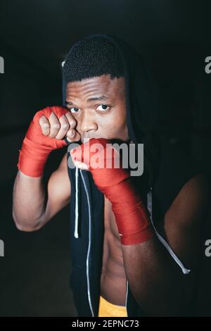 Junge starke afroamerikanische Sportler im Boxen Handwickel arbeiten Raus und Blick auf die Kamera im Gebäude Stockfoto