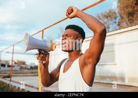 Junger wütender afroamerikanischer Rüde im Unterhemd mit Sprecherschreien Mit erhobenem Arm beim Betrachtet der Kamera Stockfoto