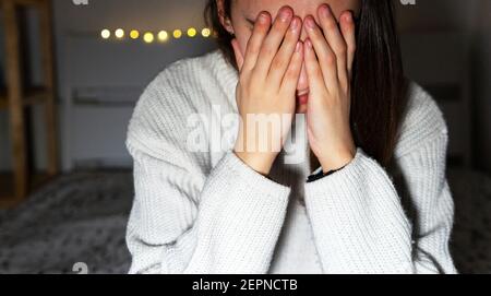 Junge Frau bedeckt das Gesicht mit den Händen, während sie allein weint Schlafzimmer zu Hause Stockfoto