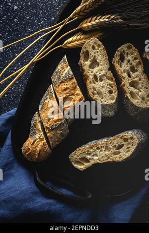 Von oben appetitlich knuspriges Brot in der Nähe von Weizenspitzen und Dunkler Stoff auf dem Tisch Stockfoto