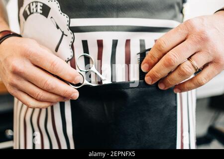 Crop unkenntlich männlichen Barbier mit Schere und Kamm in gestreift Schürze im Friseursalon Stockfoto