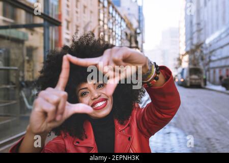 Entzückende junge afroamerikanische Frau demonstriert Rahmen Geste beim Lächeln Hell und Blick auf die Kamera Stockfoto