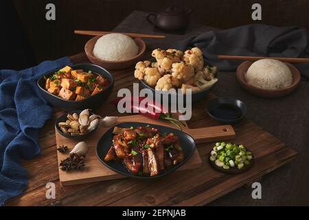 Mala Tofu und yuxiang, chinesische vegane Gerichte, begleitet von einer Schüssel mit Reis, Blumenkohl, Sojasauce und einer japanischen Teekanne auf einer hölzernen Tischdeko Stockfoto