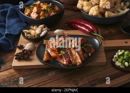 Mala Tofu und yuxiang, chinesische vegane Gerichte, begleitet von einer Schüssel mit Reis, Blumenkohl, Sojasauce und einer japanischen Teekanne auf einer hölzernen Tischdeko Stockfoto