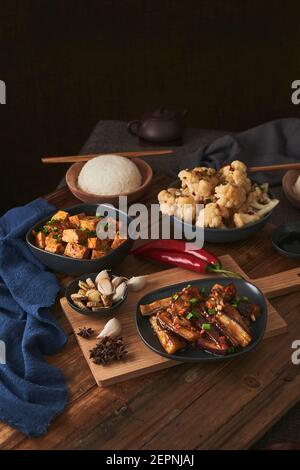 Mala Tofu und yuxiang, chinesische vegane Gerichte, begleitet von einer Schüssel mit Reis, Blumenkohl, Sojasauce und einer japanischen Teekanne auf einer hölzernen Tischdeko Stockfoto