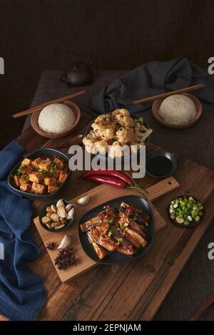 Mala Tofu und yuxiang, chinesische vegane Gerichte, begleitet von einer Schüssel mit Reis, Blumenkohl, Sojasauce und einer japanischen Teekanne auf einer hölzernen Tischdeko Stockfoto