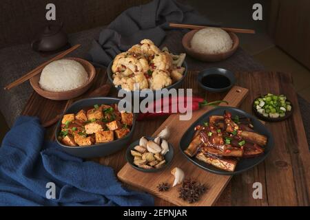 Mala Tofu und yuxiang, chinesische vegane Gerichte, begleitet von einer Schüssel mit Reis, Blumenkohl, Sojasauce und einer japanischen Teekanne auf einer hölzernen Tischdeko Stockfoto