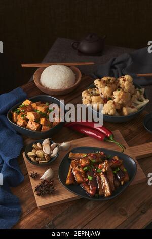 Mala Tofu und yuxiang, chinesische vegane Gerichte, begleitet von einer Schüssel mit Reis, Blumenkohl, Sojasauce und einer japanischen Teekanne auf einer hölzernen Tischdeko Stockfoto