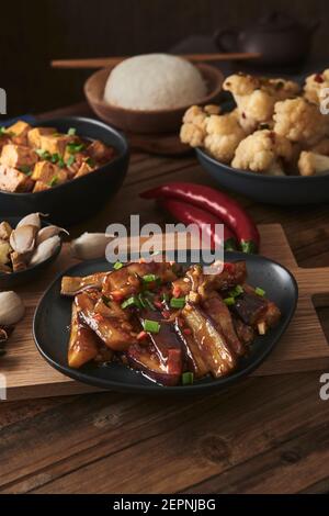 Mala Tofu und yuxiang, chinesische vegane Gerichte, begleitet von einer Schüssel mit Reis, Blumenkohl, Sojasauce und einer japanischen Teekanne auf einer hölzernen Tischdeko Stockfoto