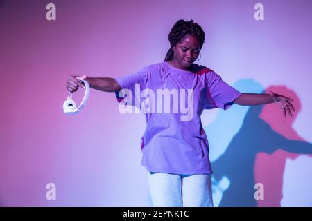 Ganzer Körper von afroamerikanischen Teenager-Mädchen mit Kopfhörern in Hand performende urbane Tanzbewegung in hellen Studio Stockfoto