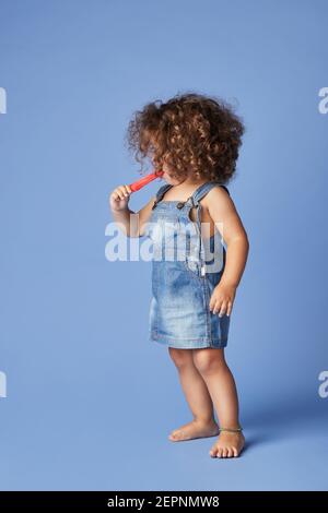 Unemotionales kleines Mädchen, das mit schmelzendem Eis vor blauem Hintergrund steht Stockfoto