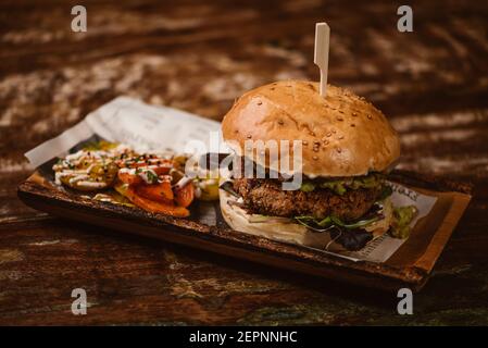 Leckerer Burger mit vegetarischem Patty und gegrillten Shiitakes zwischen den Brötchen In der Nähe Süßkartoffeln und Karotten Scheiben mit Alioli-Sauce auf Dunkler Hintergrund Stockfoto