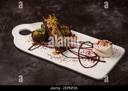 Leckere Brownies bedeckt mit Erdnussbutter und knusprigen Pistazien In der Nähe Eislöffel auf dem Teller mit Schokoladensauce Stockfoto